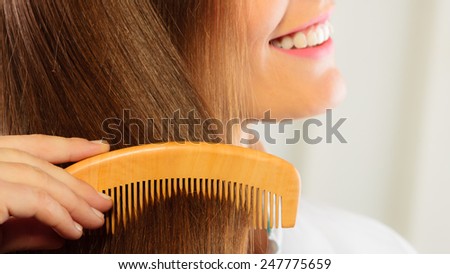 Health beauty and haircare concept - Closeup young business woman refreshing her hairstyle she combing her long brown hair with wooden comb