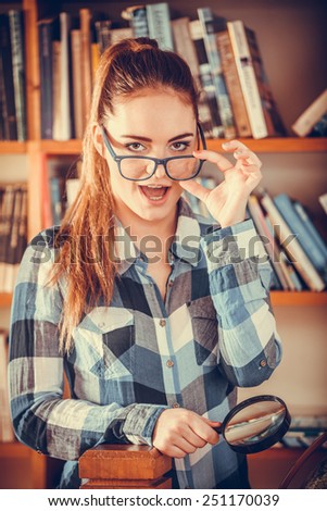 Investigation exploration education concept. Hipster funny student girl in library, woman in eyeglasses holding magnifying glass loupe
