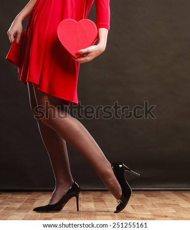 Valentines day, love, romance concept. Woman in red dress holding heart shaped gift box in hands dark gray background.