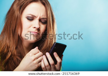 Technology and communication. Angry confused woman teenage girl texting on mobile phone, using smartphone reading sms message on blue