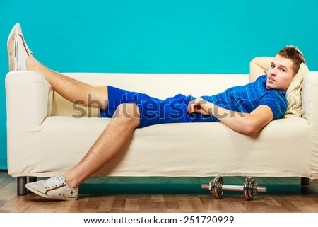 Relax after sport activity. Young man fit body relaxing on couch, dumb bell on floor