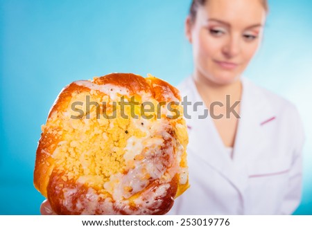Unhealthy nutrition overweight concept. Nutritionist saying no to sugary dessert. Woman doctor dietician holding sweet bun recommending non sugar diet on blue