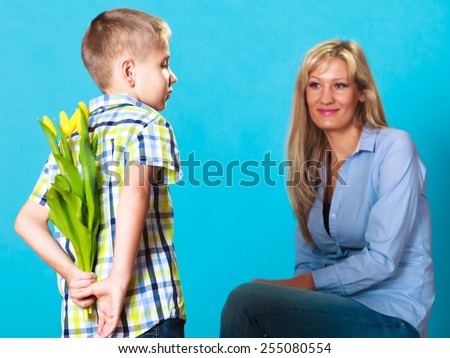 Holiday mother\'s day concept. Rear view little boy with bunch of yellow tulips behind back preparing nice surprise for his mother studio shot on blue