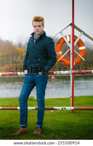 Young handsome man in full length fashion model casual style hair styling outdoor against a marine harbour