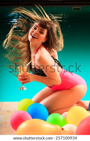 Vacation, party and fun concept. Beauty woman with tropical drink in hand and hair motion on pool with balloons.