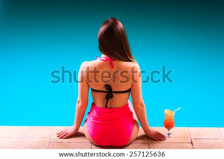 Spa relax and holidays concept. Sensual woman buttocks in swimsuit back view. Fit female body, girl sitting at poolside with cocktail glass