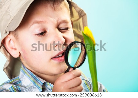 Children development. Child examining flower looking through a magnifying glass. Environmental awareness education.