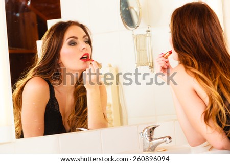 Applying make up concept. Beautiful woman with red lipstick in front of mirror in bathroom. Indoor.