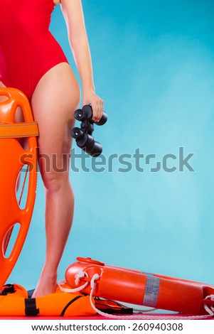 Accident prevention and water rescue. Attractive female model in lifeguard outfit on duty with binocular keeping float lifesaver equipment on blue