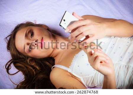 Texting and calling concept. Beauty young long haired woman lying on bad holding smartphone and texting.