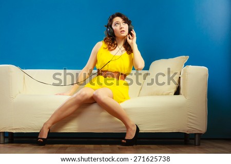 Young people leisure relax concept. Teen cute girl yellow dress in big headphones listening music mp3, sitting on couch relaxing on blue