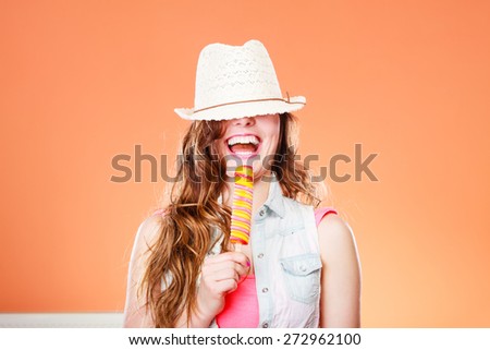 Summer vacation happiness concept. Funny cheerful woman covering eyes with straw hat eating popsicle ice cream orange background