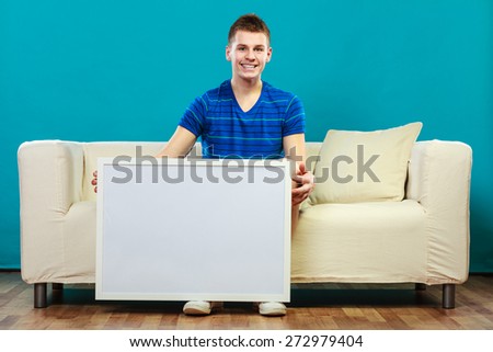 Advertisement concept. Young man sitting on sofa with blank presentation board. Male model showing banner sign billboard copy space for text on blue