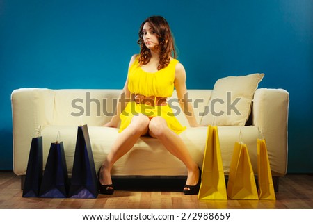Buying retail sale concept. Fashionable girl yellow dress high heels sitting on couch with shopping bags on blue