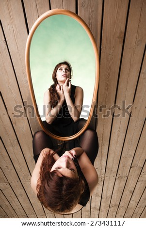 Solitude loneliness concept. Thoughtful young woman looks at the reflection in the mirror outdoors on pier