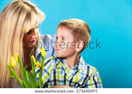 Boy celebrating mother\'s day. little child lad giving flowers yellow tulips to his mom mother studio shot on blue