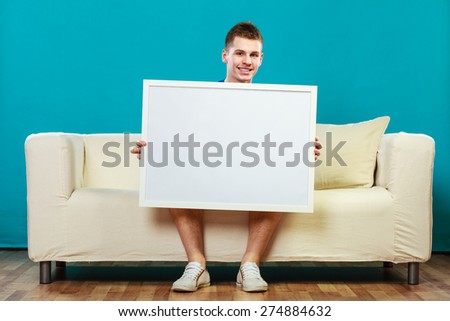 Advertisement concept. Young man sitting on sofa with blank presentation board. Male model showing banner sign billboard copy space for text on blue
