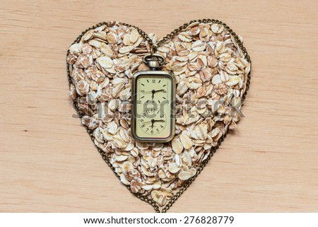 Time for dieting healthcare concept. Oat cereal heart shaped and watch on wooden surface. Healthy food for lowering cholesterol, protect heart.