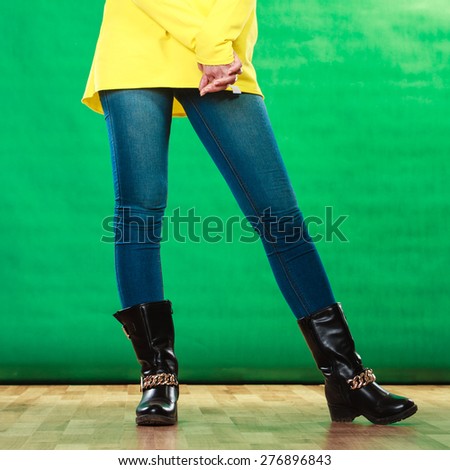 Fashion. Woman legs in denim trousers black boots casual style on green