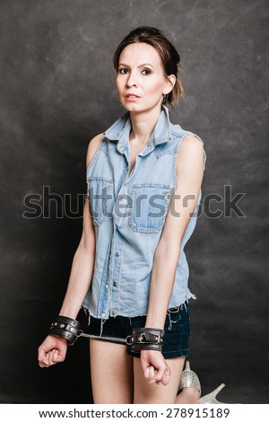 Arrest and jail. Criminal woman prisoner girl showing leather handcuffs on gray. Punishment.