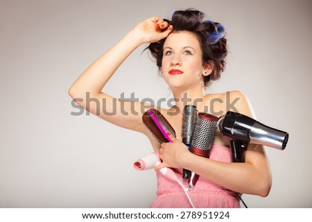 Young woman preparing for date having fun, cute girl with curlers styling hair with many accessories comb brush hairdreyer on  gray