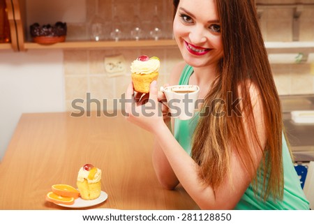 Woman drinking coffee and eating delicious gourmet sweet cream cake. Glutton girl sitting in kitchen with hot beverage and cupcake. Appetite and gluttony concept.