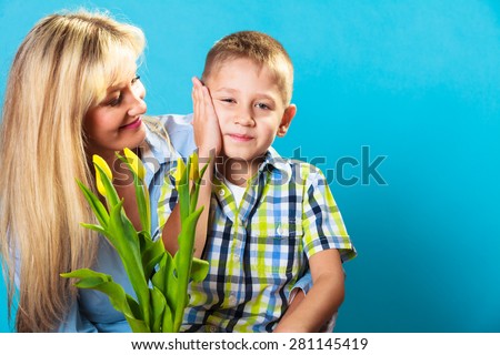 Boy celebrating mother\'s day. little child lad giving flowers yellow tulips to his mom mother studio shot on blue