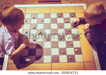 Draughts board game. Little boys clever children kids playing checkers thinking, outdoor in the park top view. Childhood and development