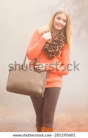 Autumn fashion. Woman fashionable girl wearing vivid clothing holding brown leather bag handbag in hand, walking in autumnal foggy park, outdoors