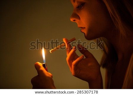Addiction. Young woman with lighter lighting up cigarette. Addicted girl smoking. Nicotine problem. Studio shot.