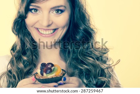 Bakery, sweet food and people concept. smiling cute woman curly hair holding fruit cake cupcake in hand yellow background