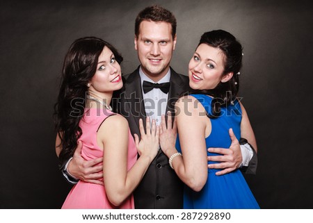 Love triangle or friendship. Portrait of smiling two women and one man wearing elegant clothes on black. Luxury party.