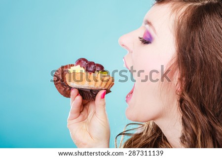 Sweet food indulging and fattening concept. Woman face profile wide open mouth eating cake cupcake blue background