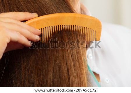 Hair care concept. Closeup straight brown healthy shiny hair and hand holding wooden comb, combing hairstyle