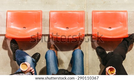 Sport competitions, recreation and relax. Row of plastic chairs and human legs in football stadium. Hot drink disposable cups with tea and coffee in hands.