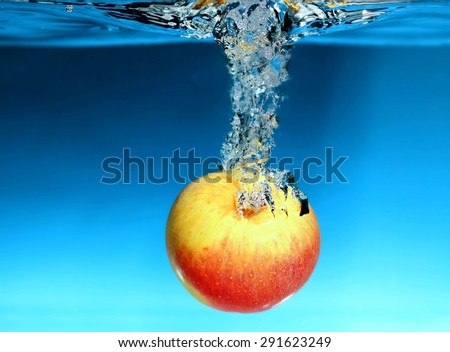 Yellow red apple in the water splash over blue background. Healthy food and active life.