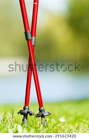 Nordic walking equipment. Closeup of red sticks on the green grass in the park. Active and healthy lifestyle.