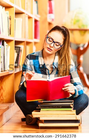 Education school concept. Clever female student hair ponytail girl blue glasses sitting on floor in college library with stack books. Indoor