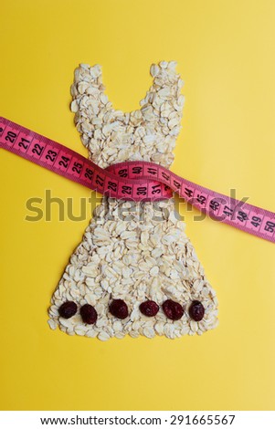 Dieting healthy eating slim down concept. Female dress shape made from oatmeal dried fruit with measuring tape around thin waist on yellow