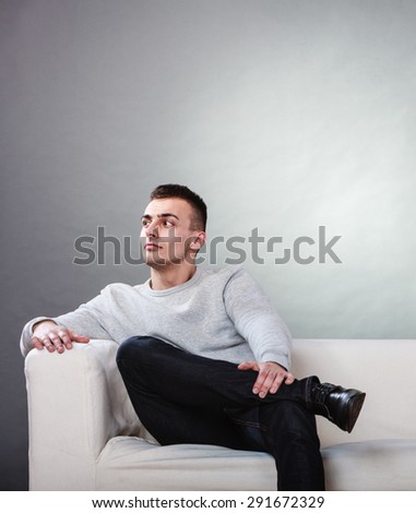 Fraught, uptight, bored man husband waiting for shopping woman wife at shop. Upset, dissatisfied boyfriend sitting on couch with leg over leg.