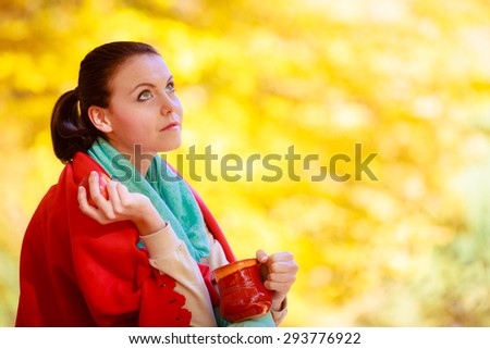 Happiness carefree and nature. Young woman relaxing in the autumn park enjoying hot drink coffee or tea, holding red mug with warm beverage. Yellow leaves background