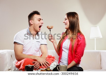 Smiling woman feeding happy man with cake. Wife and husband eating caloric food.