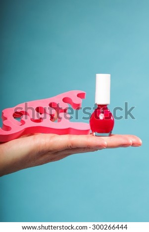 Pedicure accessories red nail polish and pink toe separators on female hand blue background