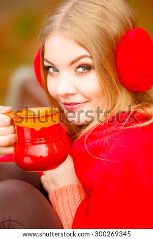 Happiness carefree and fall concept. Young happy woman relaxing in the autumn park on bench enjoying hot drink holding red mug with warm beverage. Orange leaves background