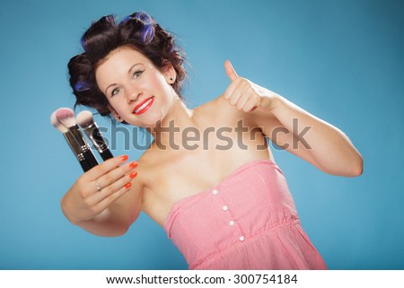 Cosmetic beauty procedures and makeover concept. Woman in hair rollers holding makeup brushes set making thumb up gesture on blue