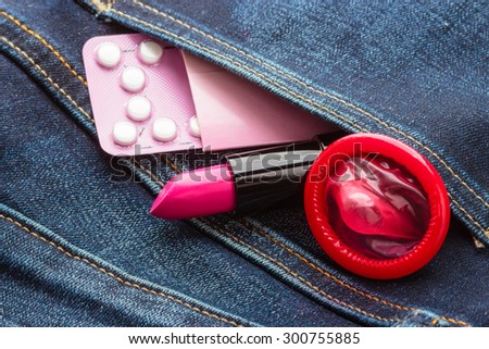 Healthcare medicine, contraception and birth control. Closeup oral contraceptive pills, condom and pink lipstick in denim pocket.