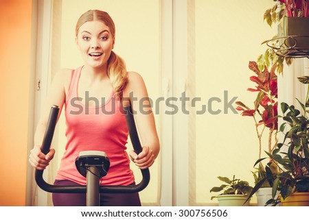 Active young woman working out on exercise bike stationary bicycle. Sporty girl training at home. Fitness and weight loss concept. Instagram filtered.