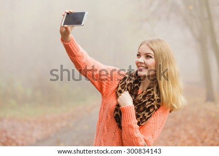 Happy fashion woman in fall autumn park taking selfie self photo picture. Pretty joyful young girl in sweater pullover with handbag photographing.