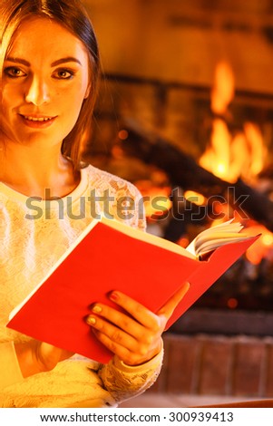 Woman reading book at fireplace. Young girl heating warming up and relaxing. Winter at home.