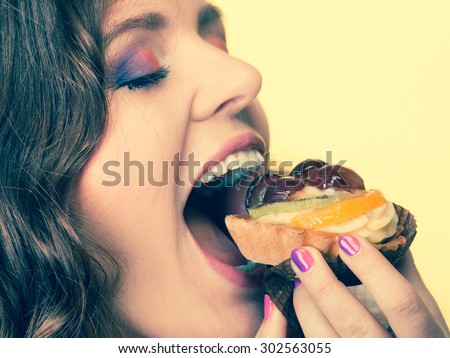 Sweetness and happiness concept. Closeup cute woman curly hair eating fruit cake cupcake face profile yellow background